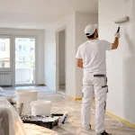 Pintor profesional pintando un piso mientras se calculan costes de pintura y mano de obra